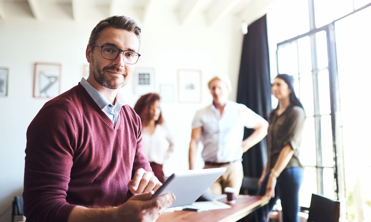 Office setting, man holding a tablet, with people in the background.